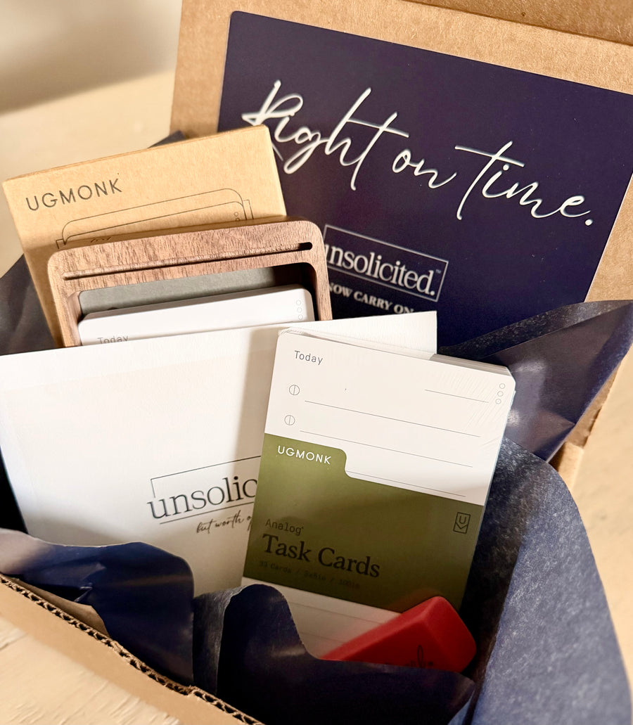 Alt text: Open unsolicited. care package with a letter, wooden card organizer, and task cards wrapped in navy tissue.